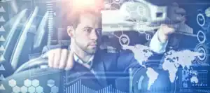 A man in a suit sits in a car, touching a transparent digital interface with various futuristic charts, maps, and data icons overlaid, suggesting advanced technology or smart driving features.