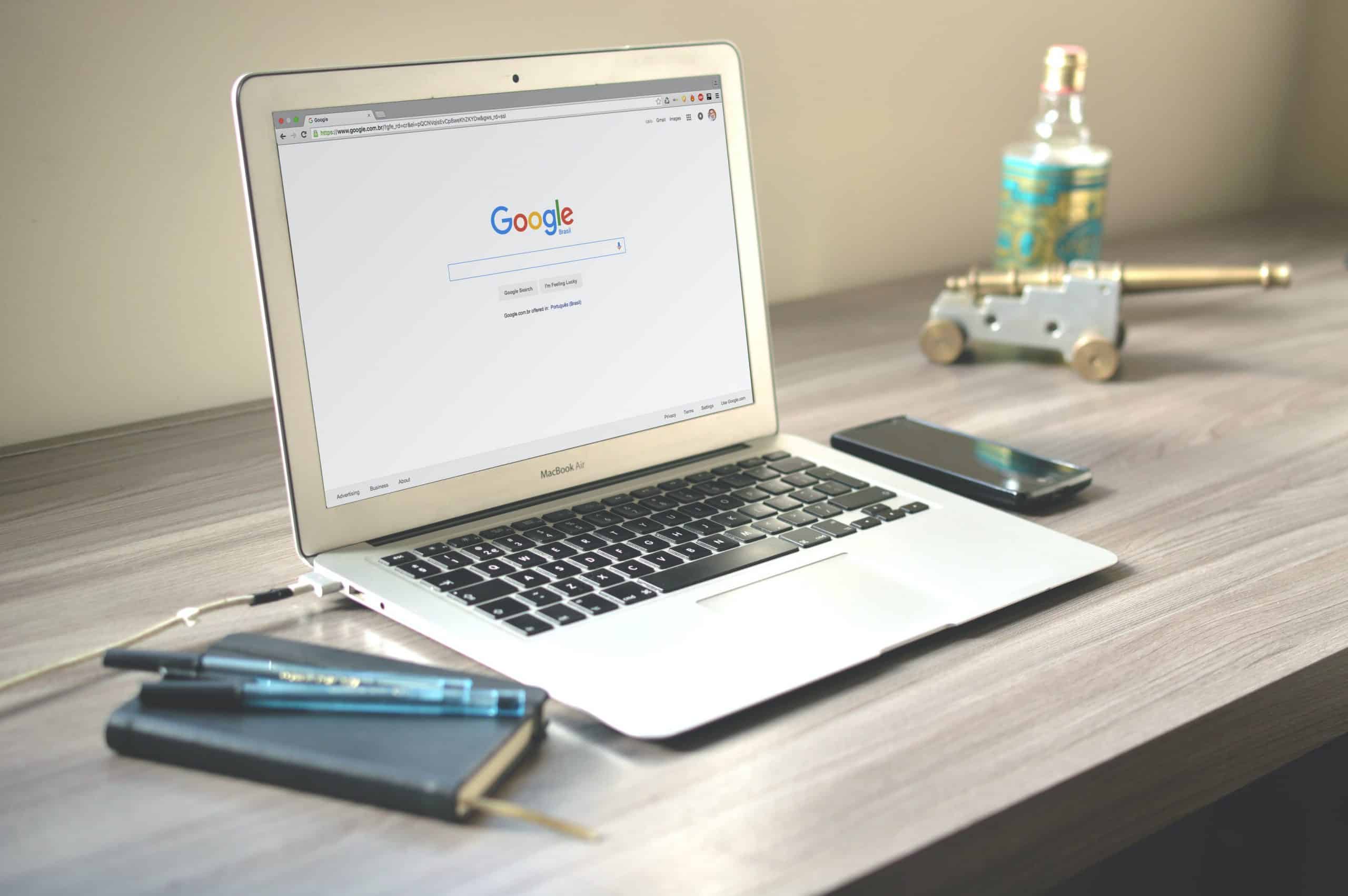 A silver laptop on a wooden desk, showing Google’s search engine page.