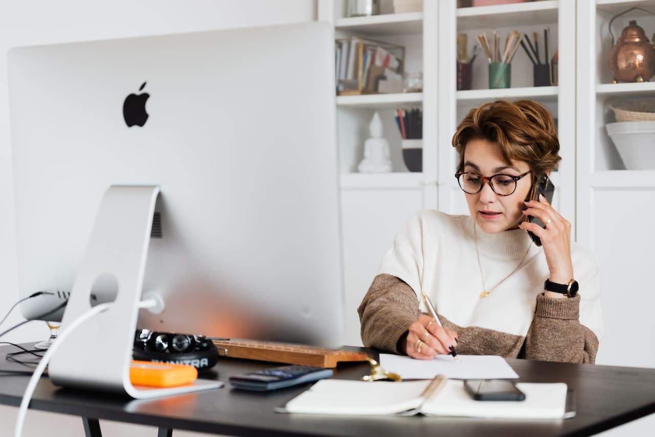 A lady using a phone while looking at the computer.