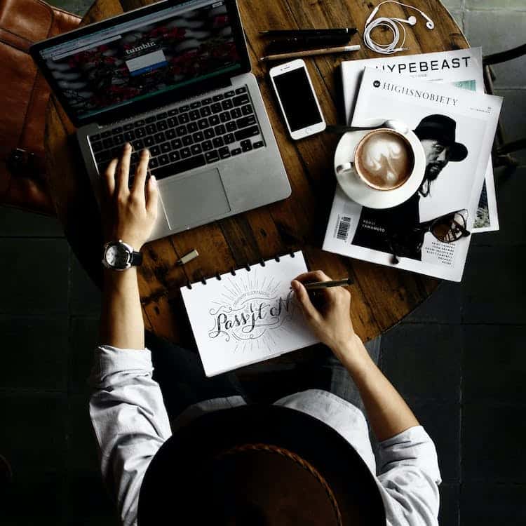 A person working on a laptop as they draw on a sketch pad.