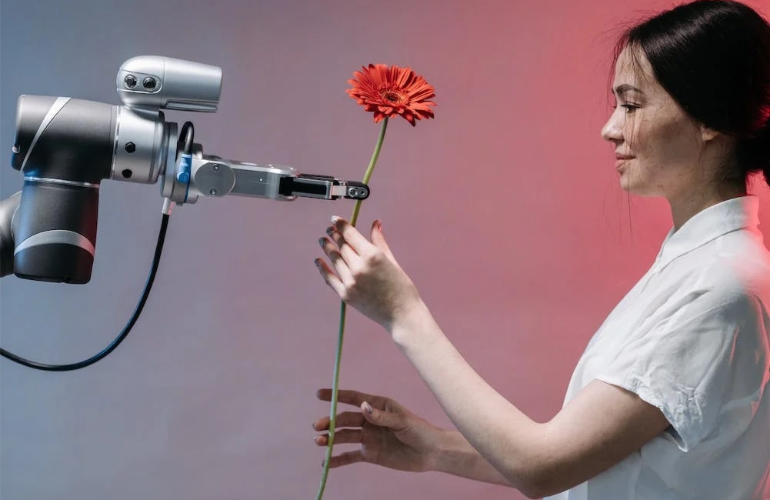 A robotic hand giving a flower to a smiling woman.