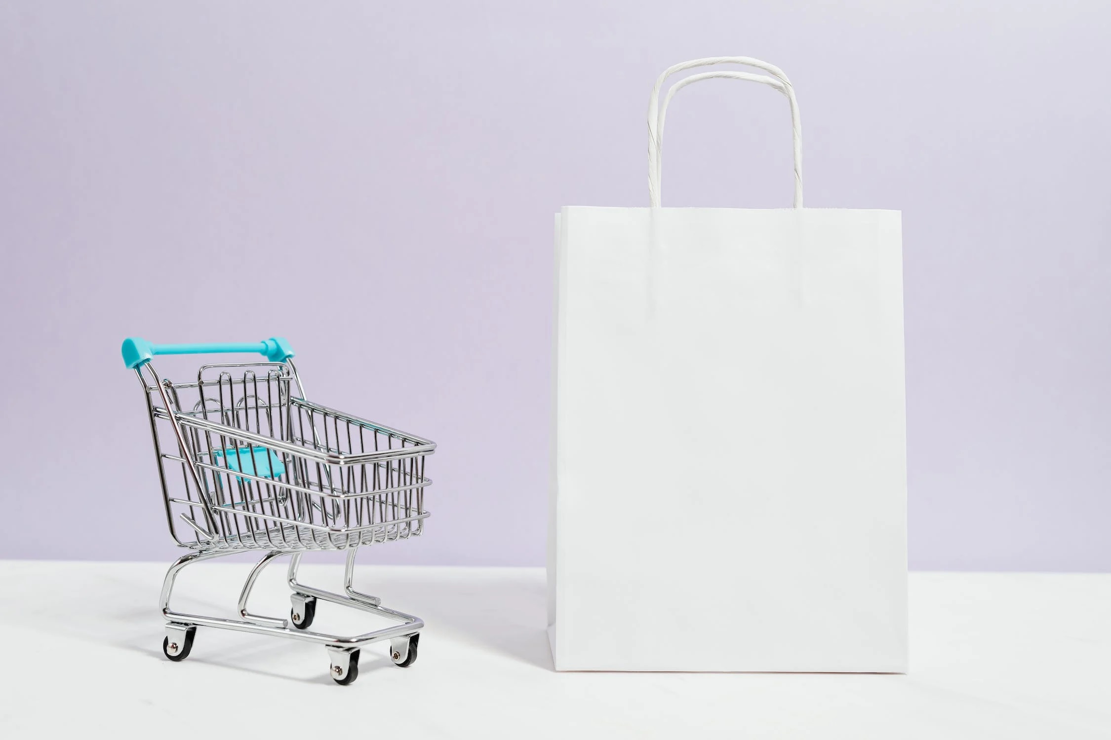 A miniature shopping cart next to a white paper bag.