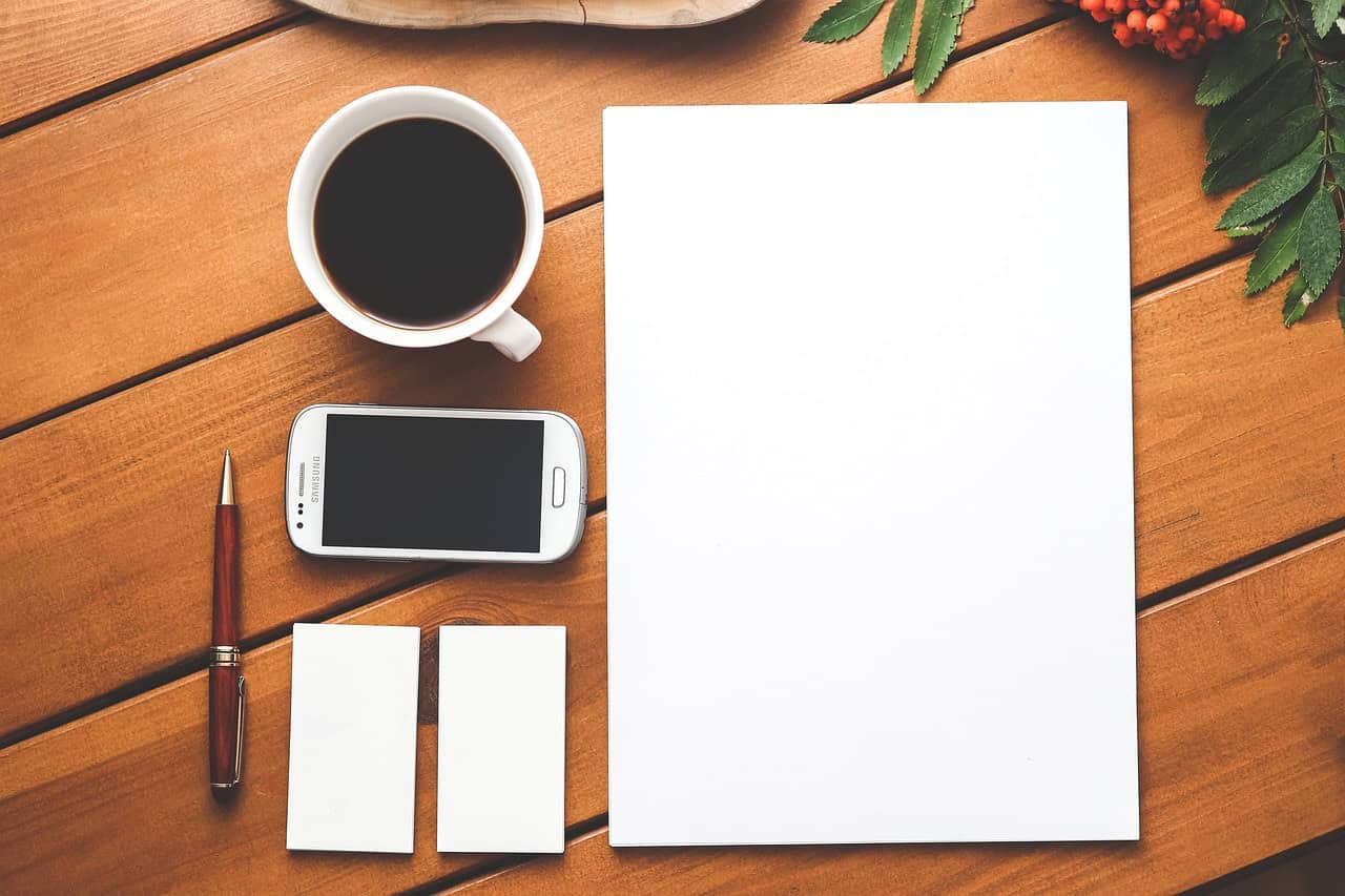 A notebook on a desk next to papers, a smartphone, and a cup of coffee.