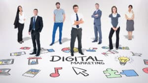 Seven business professionals stand confidently around the words Digital Marketing, surrounded by colorful digital and marketing icons on a white background.