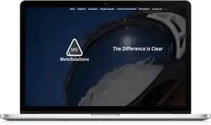 A laptop displays the MotoSolutions website homepage, featuring their logo, a mountain reflected in goggles, and the slogan The Difference is Clear over a dark background.