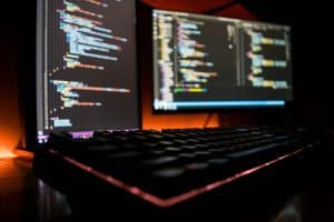 Backlit keyboard in front of dual monitors displaying code, representing website development